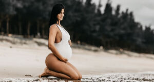 A pregnant woman posing for a photoshoot on a beach.